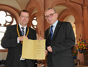 Uni-Präsident Alfred Forchel überreicht die Urkunde der Verdienstmedaille "Bene Merenti" an Prof. Dr. Dr. Karlheinz Müller (rechts). (Foto: Gunnar Bartsch)
