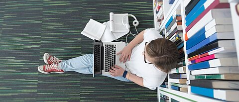 female student study in school library, using tablet and searching for information’s on internet. Listening music and lessons on white headphones