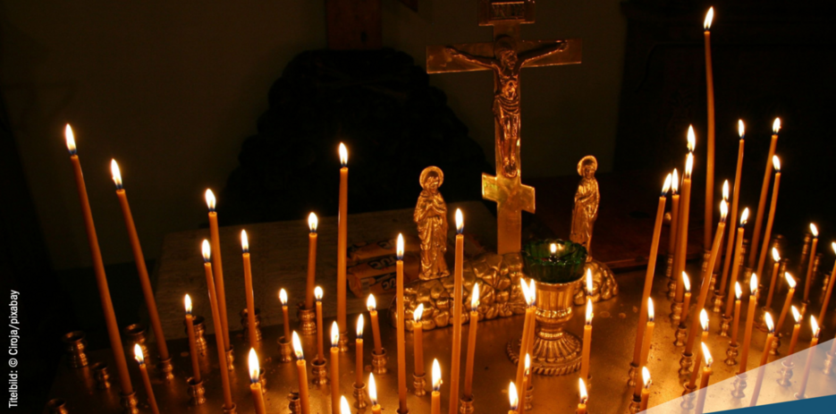 Kerzen in einem Kerzenständer vor einem Kreuz