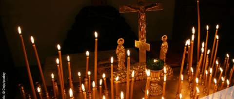 Kerzen in einem Kerzenständer vor einem Kreuz