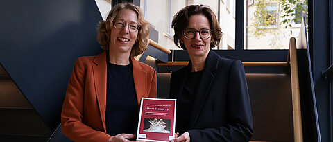 Veronika Bachmann und Barbara Schmitz stehen im Treppenhaus und präsentieren das Buch Update-Exegese 2.3