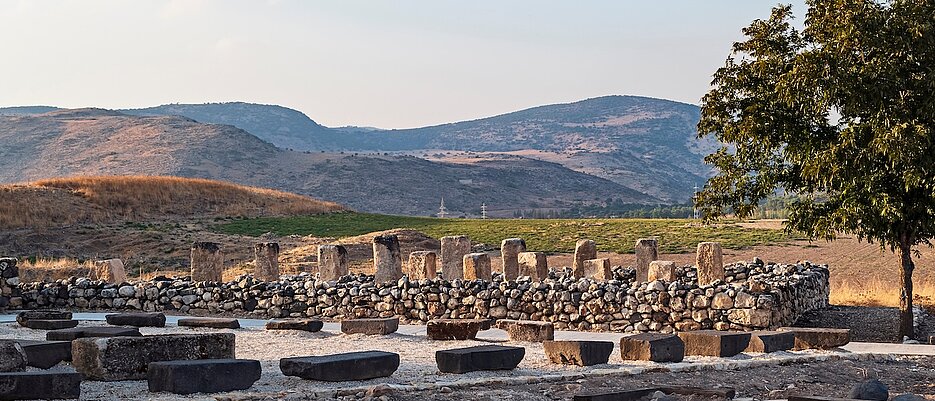 ruins of an israelite stone storehouse made with pillars and columns at the tel hazor archaeological park in israel with the canaanite city and kibbutz ayelet shahar in the background