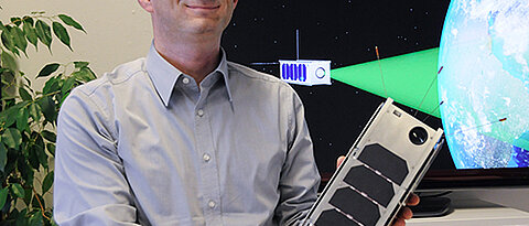 Hakan Kayal mit einem Modell das Nanosatelliten, der voraussichtlich 2019 im Rahmen der SONATE-Mission in den Orbit geschickt werden soll. (Foto: Robert Emmerich)